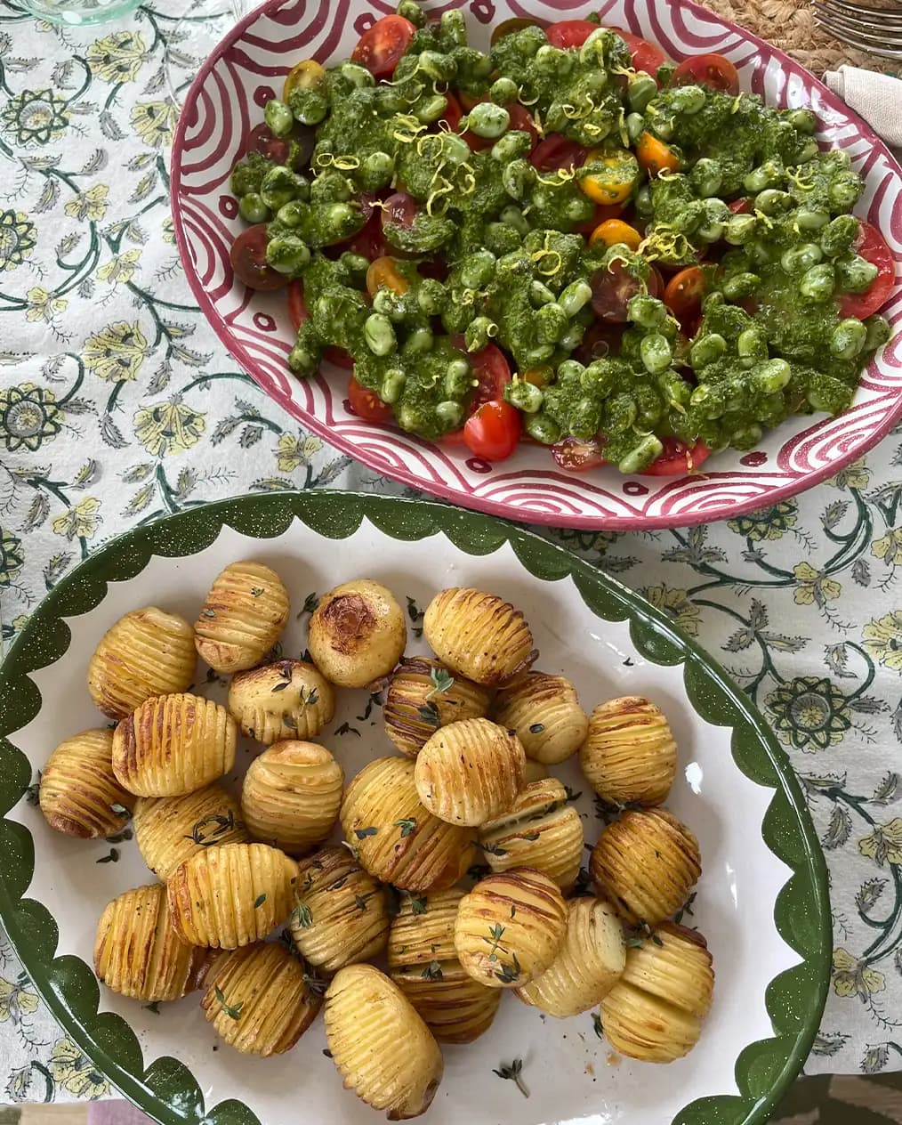 Potatoes and salad served on tableware wedding presents, hand-painted platters, placed on a floral tablecloth.