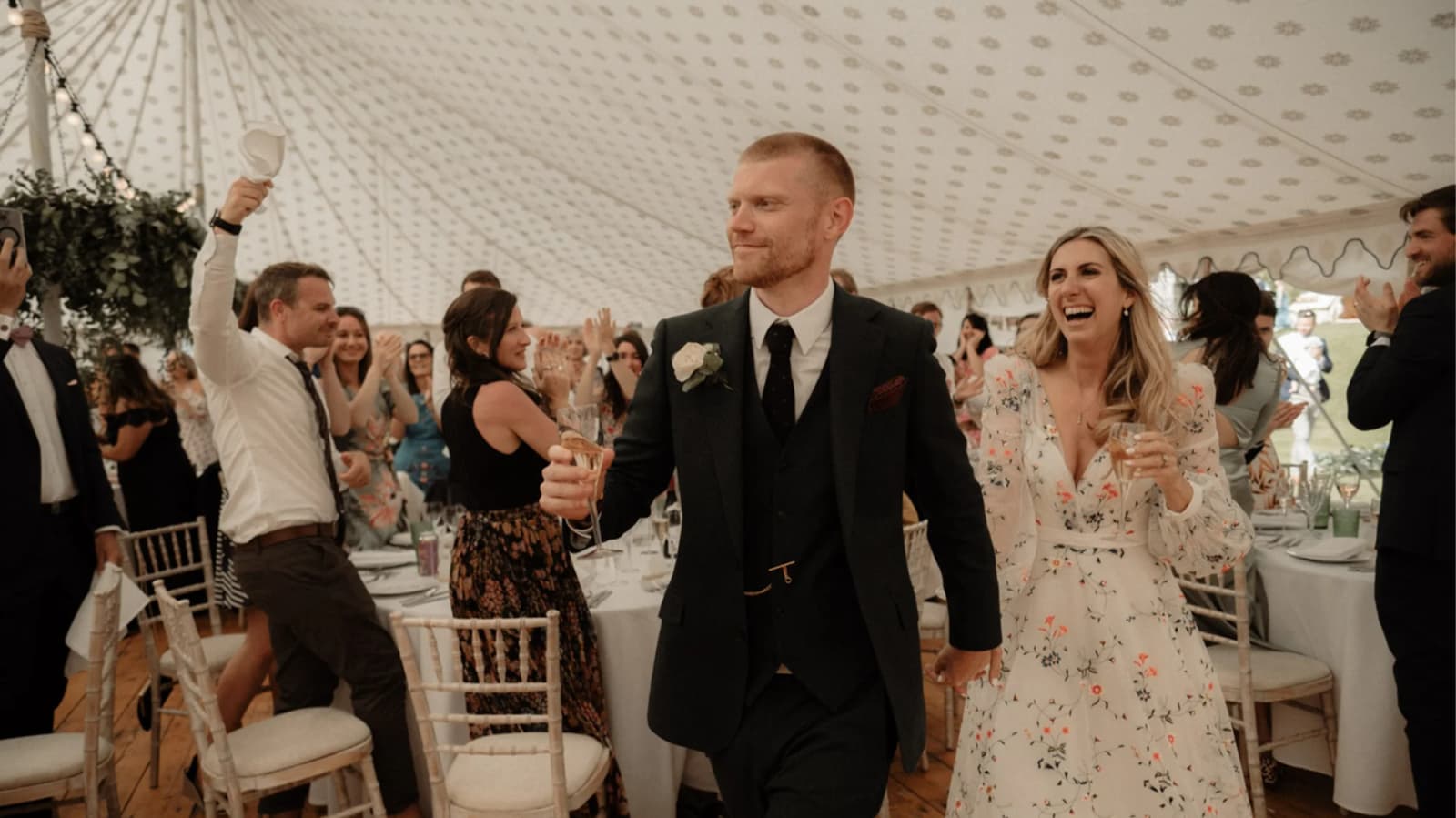 Bride and groom being toasted while they walk through their wedding marquee